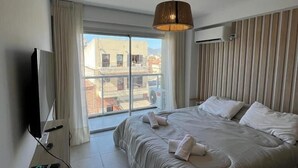 Une chambre d’hôtel avec un grand lit, une télévision, une fenêtre avec des rideaux et une vue sur les bâtiments environnants.