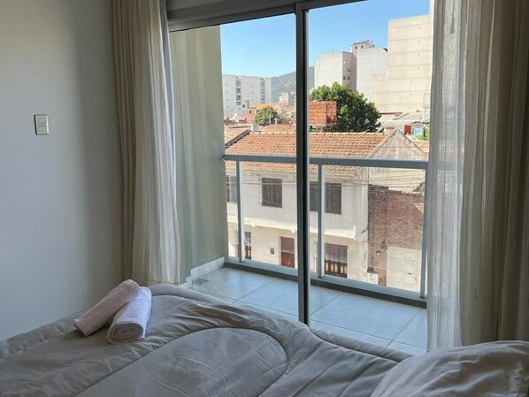 A bedroom with a large window, a bed, and a view of buildings outside.