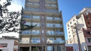 Un immeuble à plusieurs étages doté de balcons, une voiture garée et une devanture de magasin bien visible.