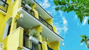 A multi-story yellow building with balconies, a clear blue sky, and green foliage.