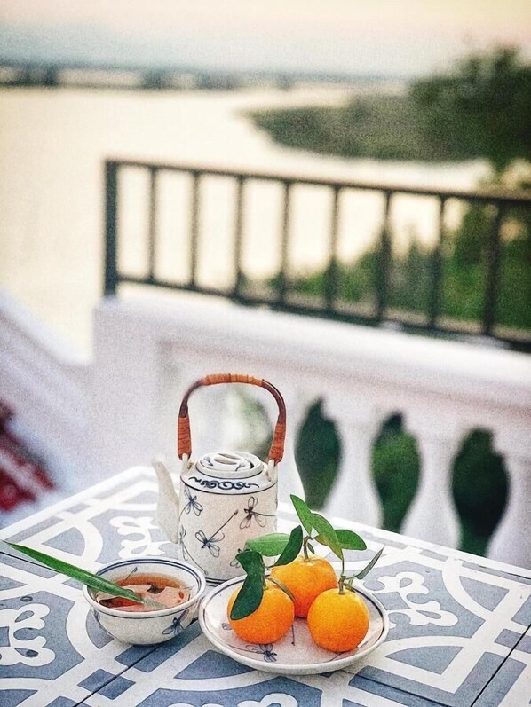 A table with a teapot, a bowl of tea, and a plate with oranges on a patterned tablecloth.
