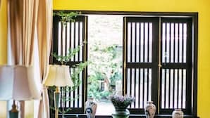 A room with a yellow wall, a ceiling fan, a sofa, a table, and a window with vertical blinds.
