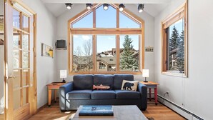 A cozy living room with a large window, a blue sofa, a coffee table, and a fireplace.