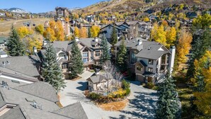 A residential area with houses surrounded by autumn foliage, a ski lift, and a mountainous backdrop.