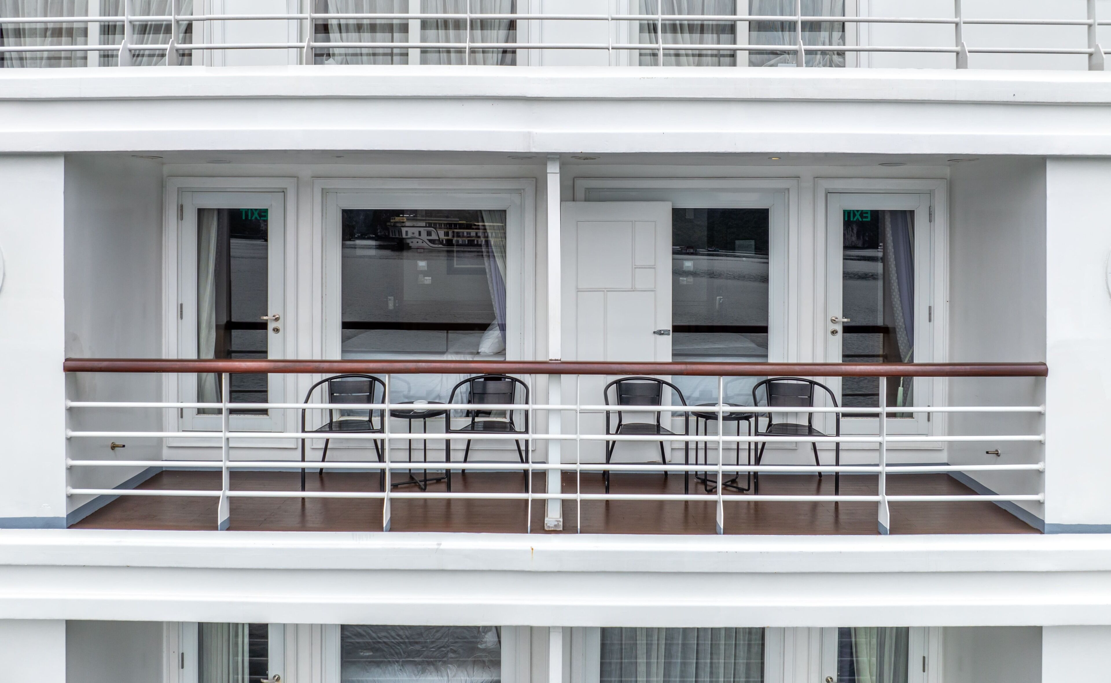 A balcony with four chairs and a table, white doors, and a railing.