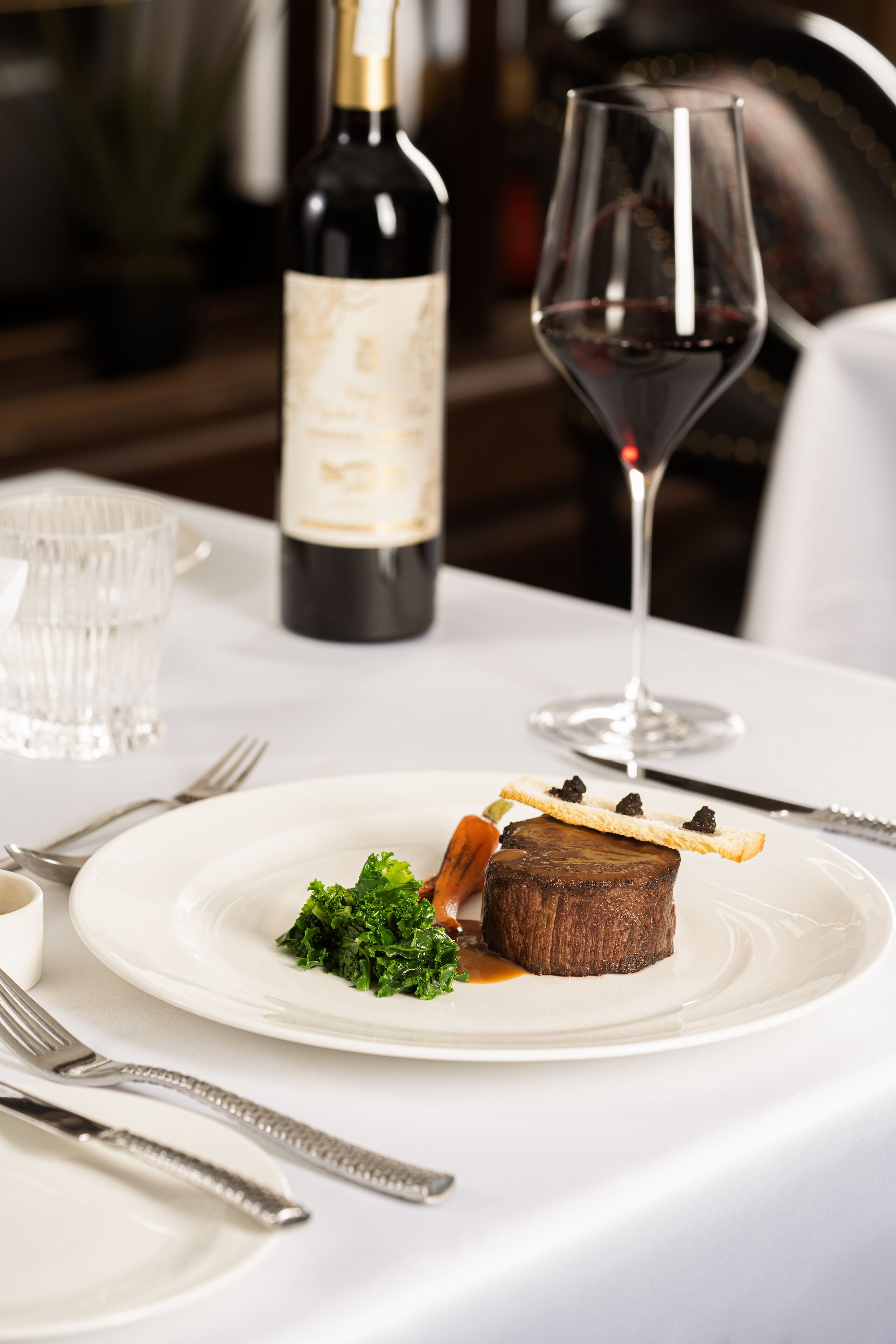 A dining table with a plate of food, a wine bottle, and a wine glass.