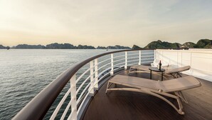 A deck with a curved railing, a table with a bottle, and a lounge chair. - Ambassador Signature Cruise - Lan Ha Bay (Bai Chay)