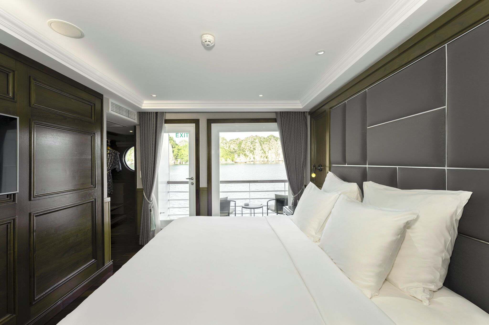 A hotel room with a large bed, a dark wood wardrobe, and a view of the outdoors.