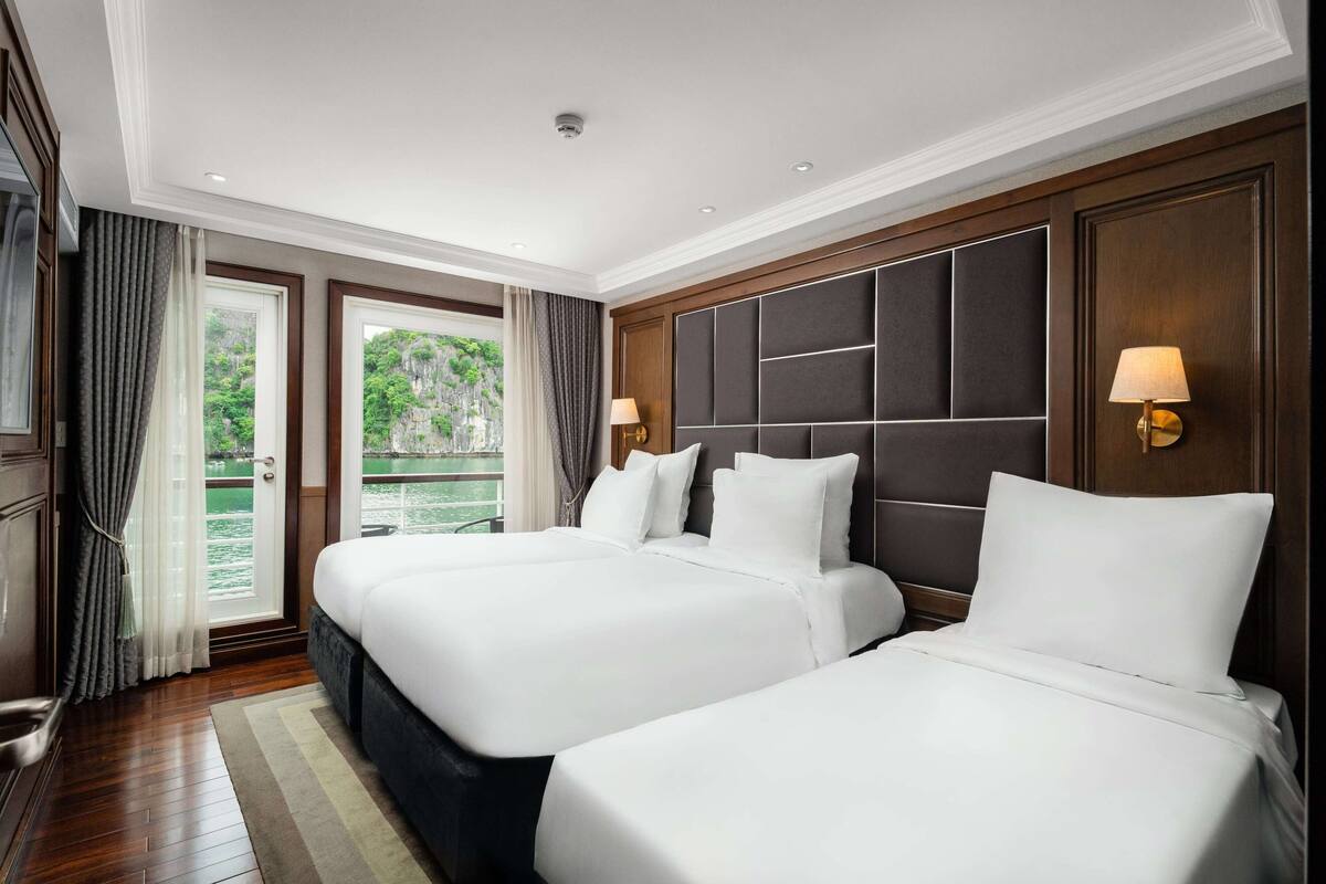 A hotel room with two beds, a view of greenery, and a balcony.