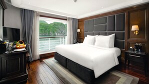 A spacious hotel room with a large bed, a television, a desk with a lamp, and a view of a body of water. - Ambassador Signature Cruise - Lan Ha Bay (Bai Chay)