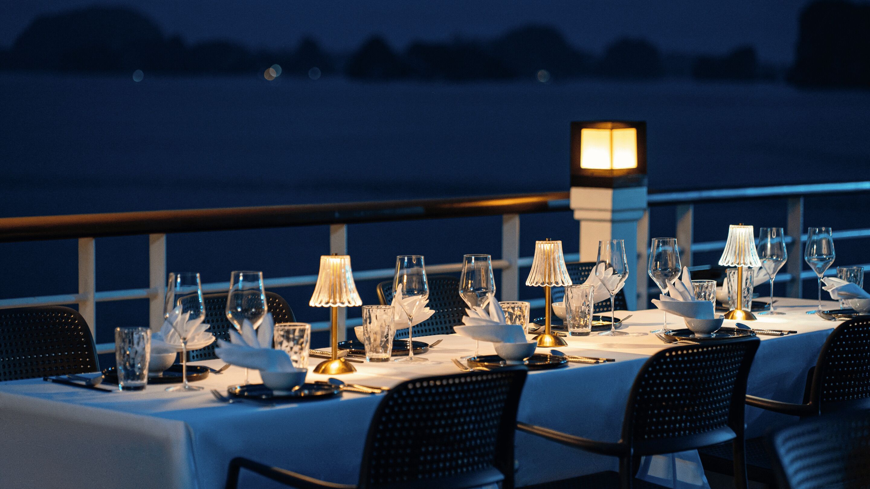 A table set for dining with a view of the water at night.