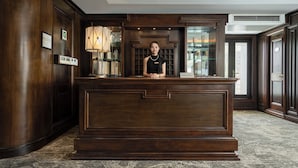 En receptionsdisk med en kvinna som står bakom den, inramad av mörka träpaneler och en stor lampa.