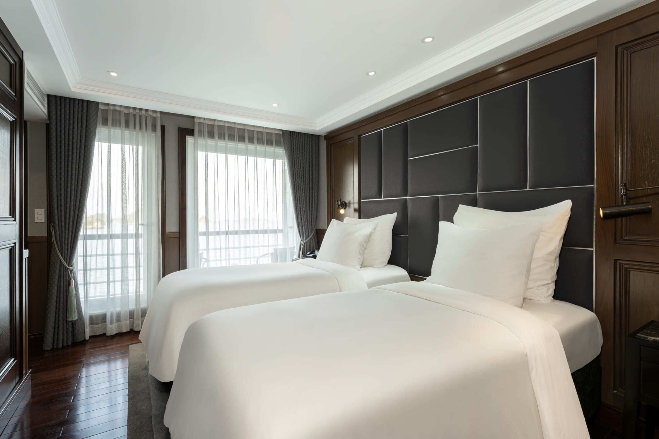 A hotel room with two beds, a large window with curtains, and a dark headboard.