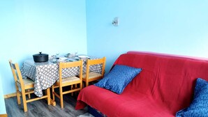 Una habitación con un sofá rojo, dos sillas de madera, una mesa dispuesta para comer y una alfombra estampada.
