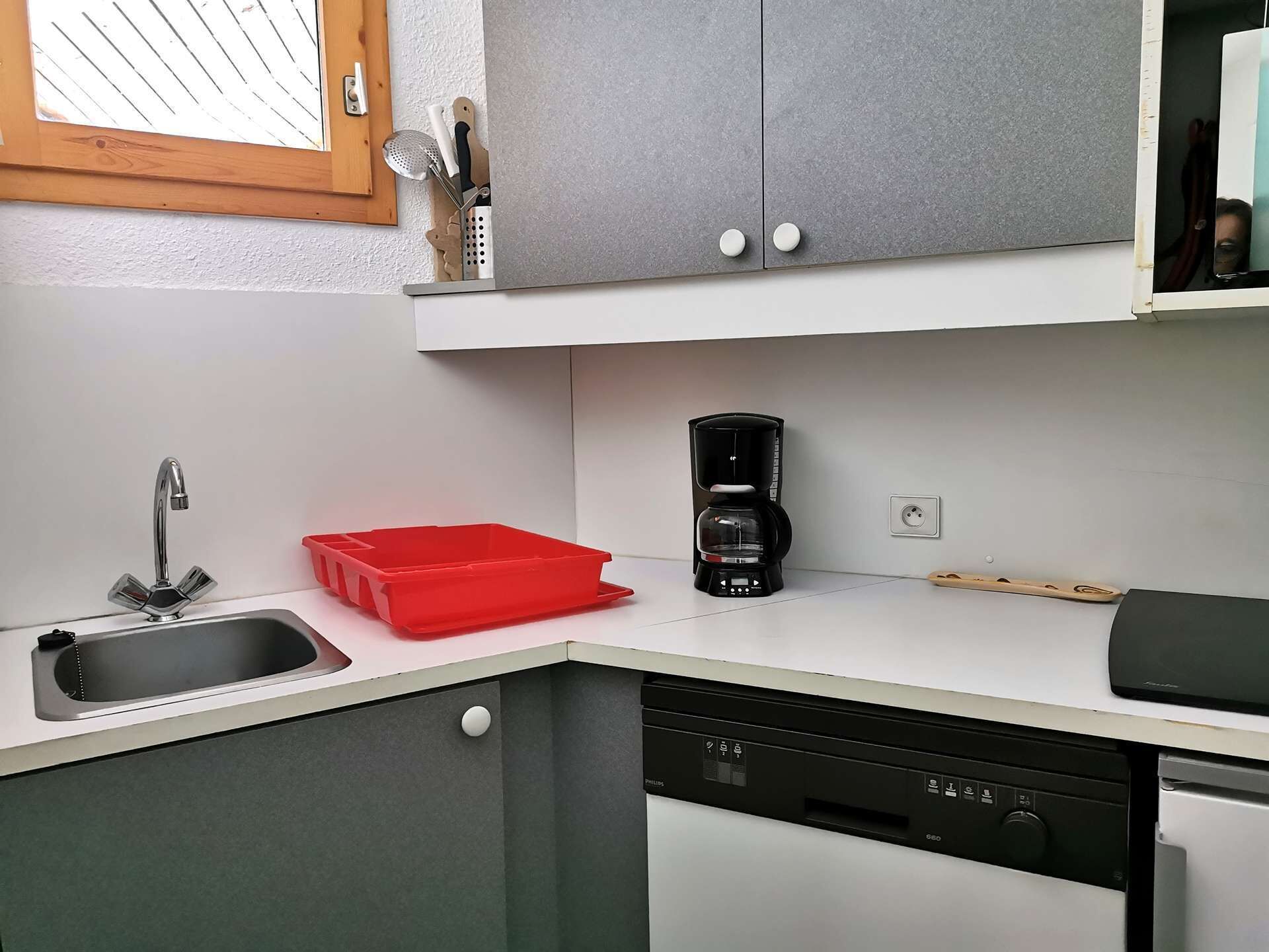 Une cuisine moderne équipée d’un évier, d’un bac de rangement rouge, d’une machine à café et d’un lave-vaisselle.