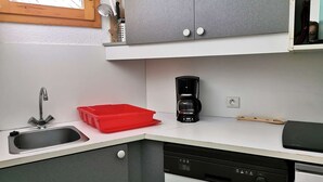 Una cocina moderna con un lavamanos, un contenedor rojo de almacenamiento, una cafetera y un lavavajillas.
