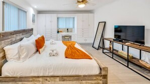 A bedroom with a wooden bed, white bedding, a television, and a desk with a chair.