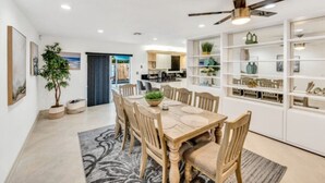 A spacious dining area with a wooden table and chairs, a ceiling fan, and a view into the kitchen.