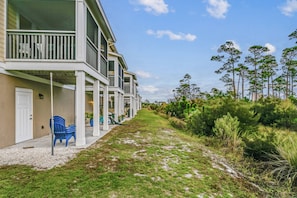A row of modern multi-story buildings with balconies, a gravel pathway, and surrounding greenery.