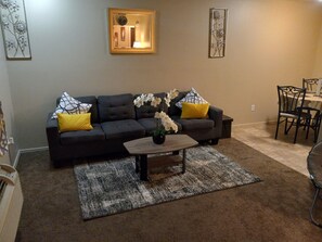 A living room with a dark grey sofa, yellow and patterned cushions, a wooden coffee table with a vase of white flowers, and a rug. - The Great Place in Fayetteville, less than a mile to the University of Arkansas. (Fayetteville)