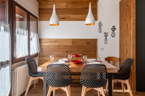 Un espace repas comprenant une table en bois, quatre chaises, des suspensions blanches et des œuvres d’art murales.