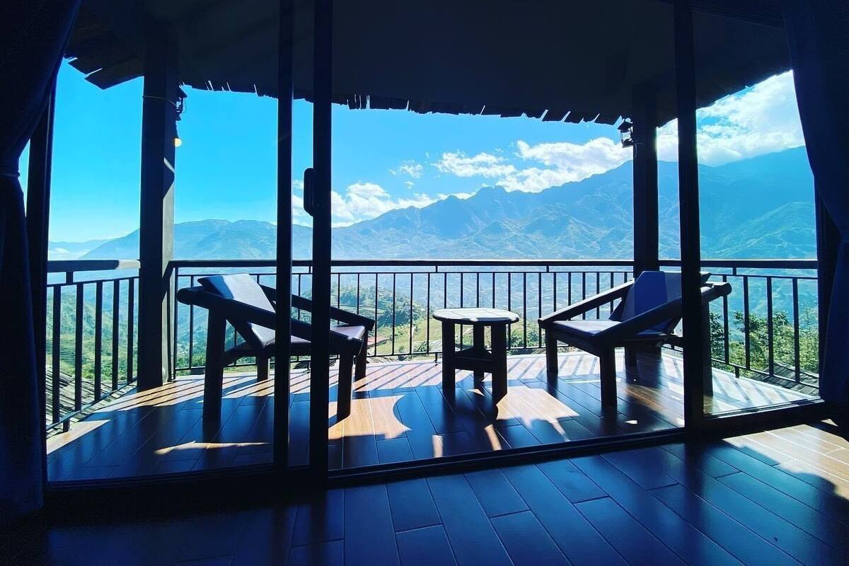 A balcony with two chairs and a small table, overlooking a mountainous landscape.