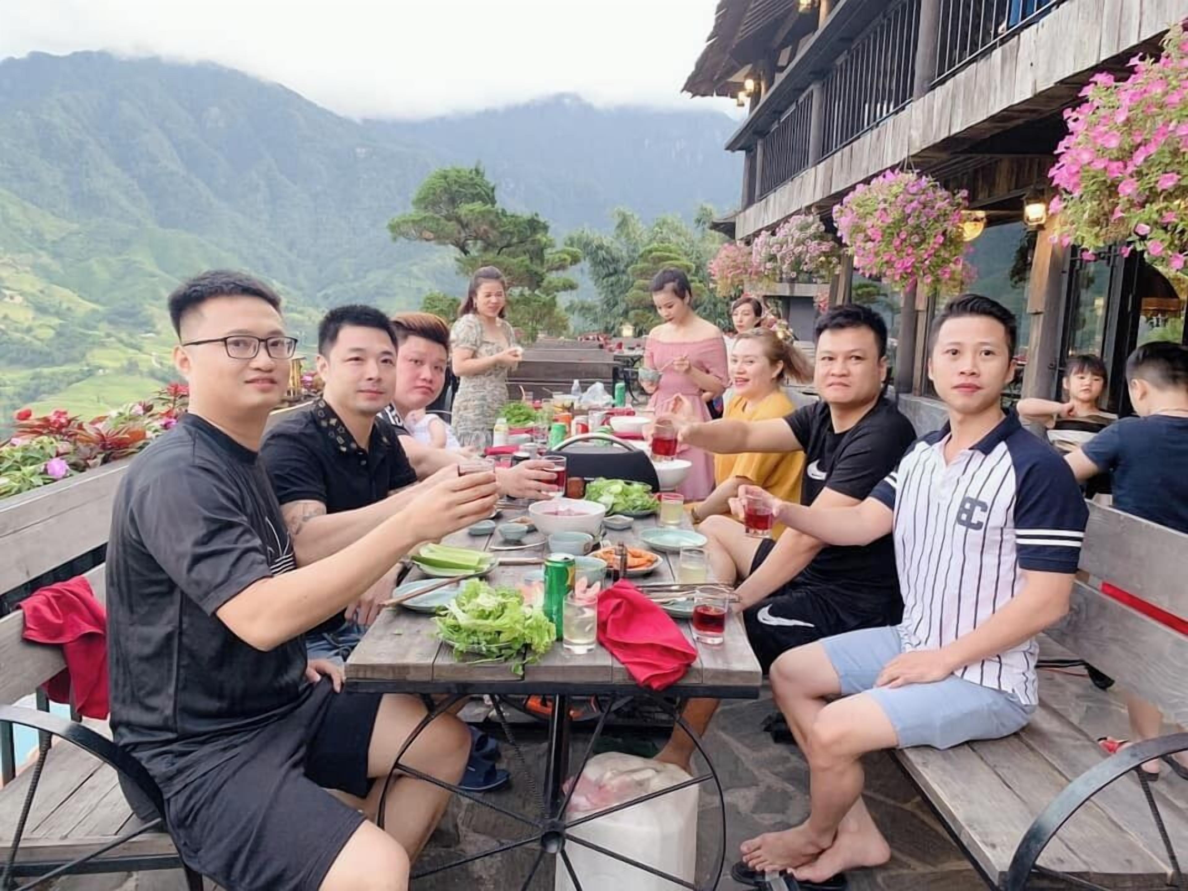 Un grupo de personas cenando al aire libre con montañas al fondo.