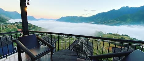 Un balcón con vistas a un valle y montañas, con una mesa y dos sillas.