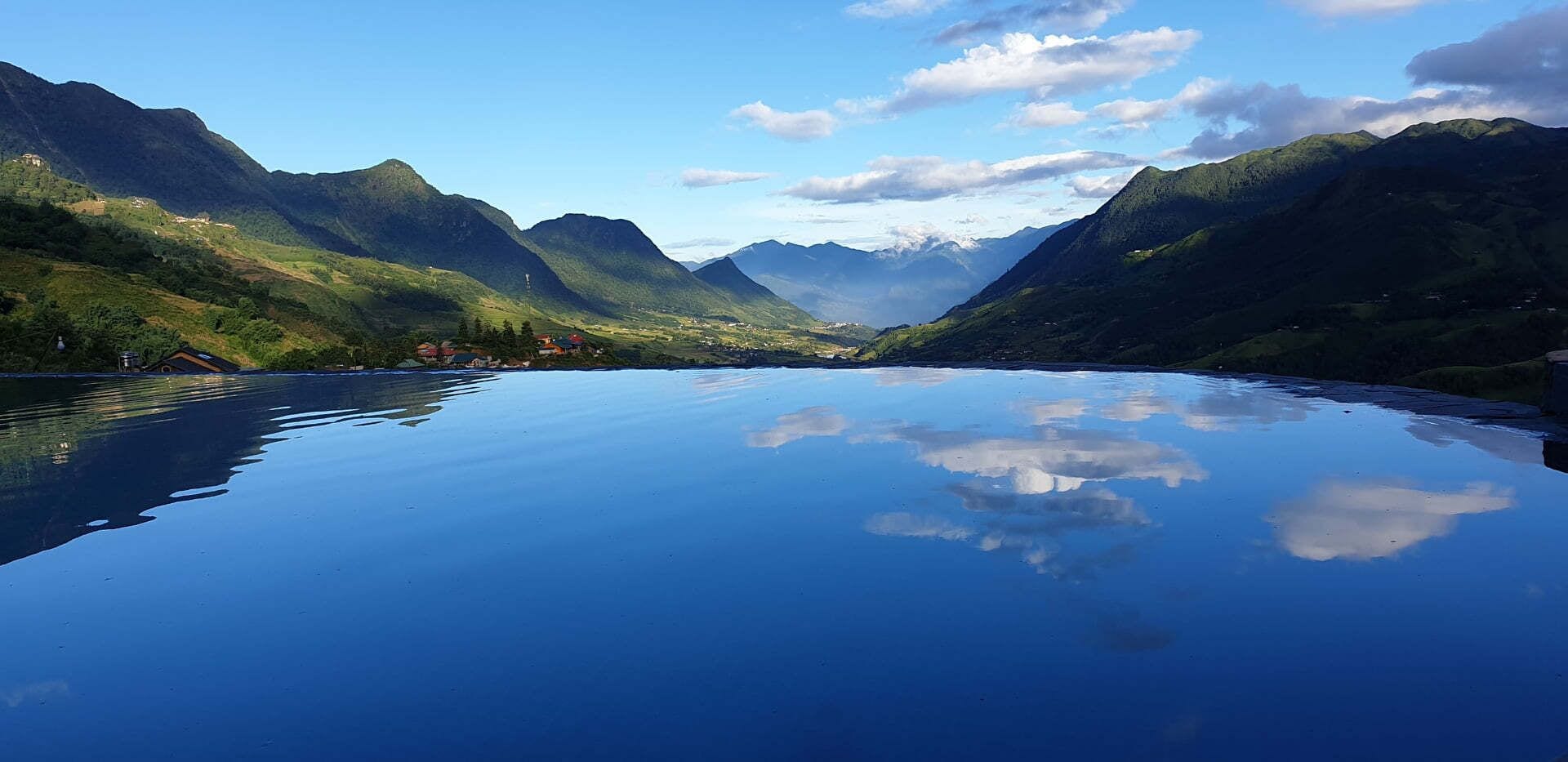 A serene lake with mountains in the background and a clear reflection of the sky and clouds.