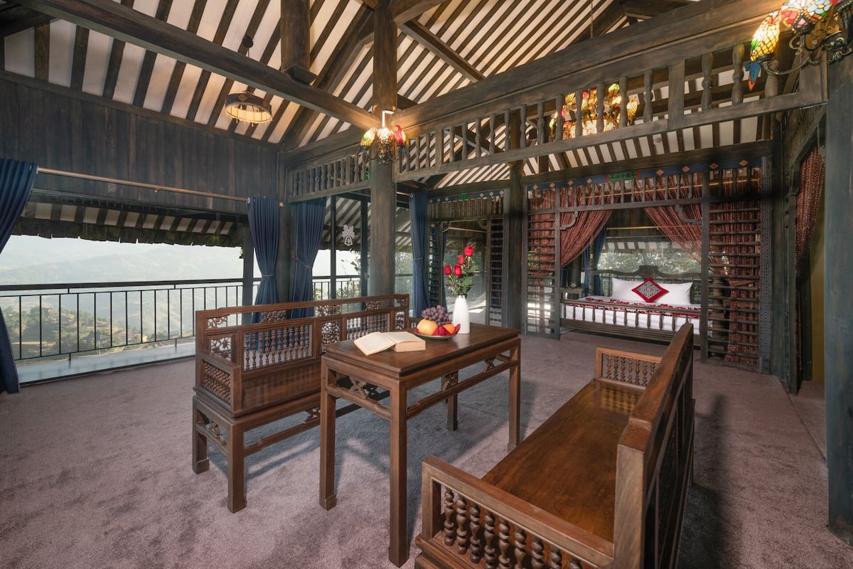 A room with a wooden table, two chairs, a sofa, and a large window overlooking a scenic view.
