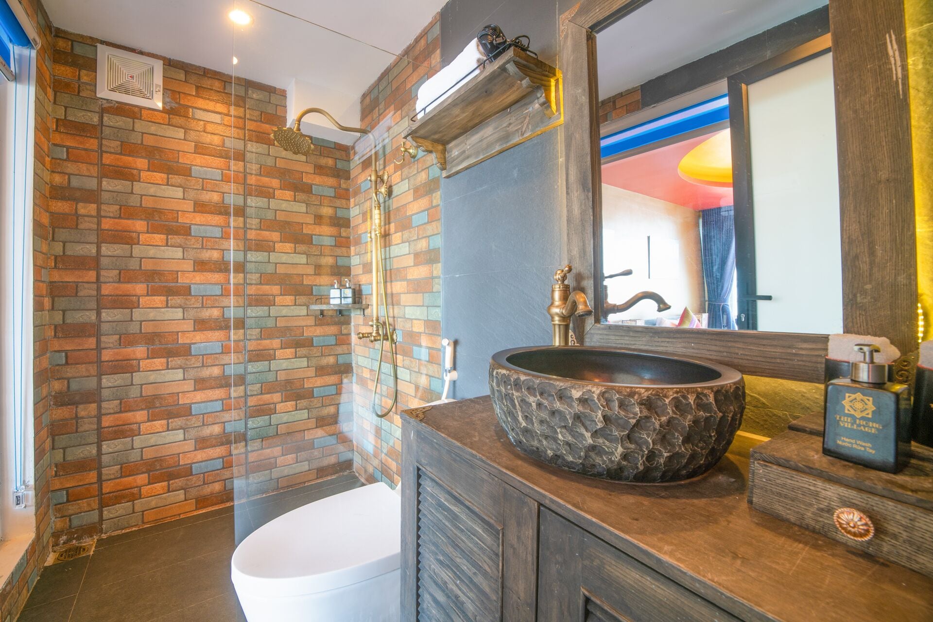 A bathroom with a brick wall, a white toilet, a stone sink, and a mirror.