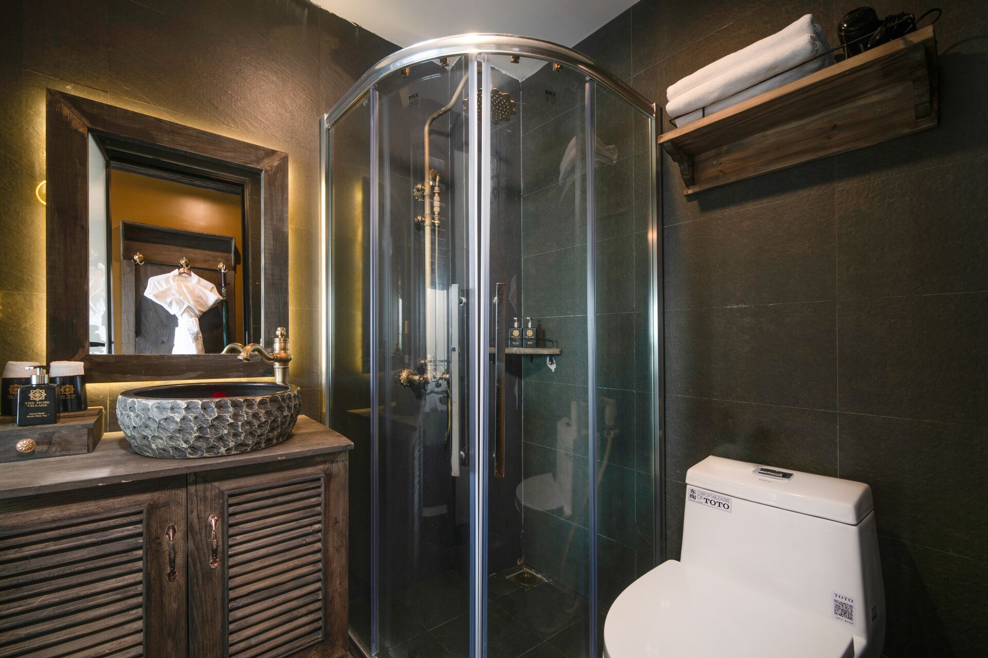 Un baño con ducha de vidrio, lavabo de piedra, tocador de madera y retrete.