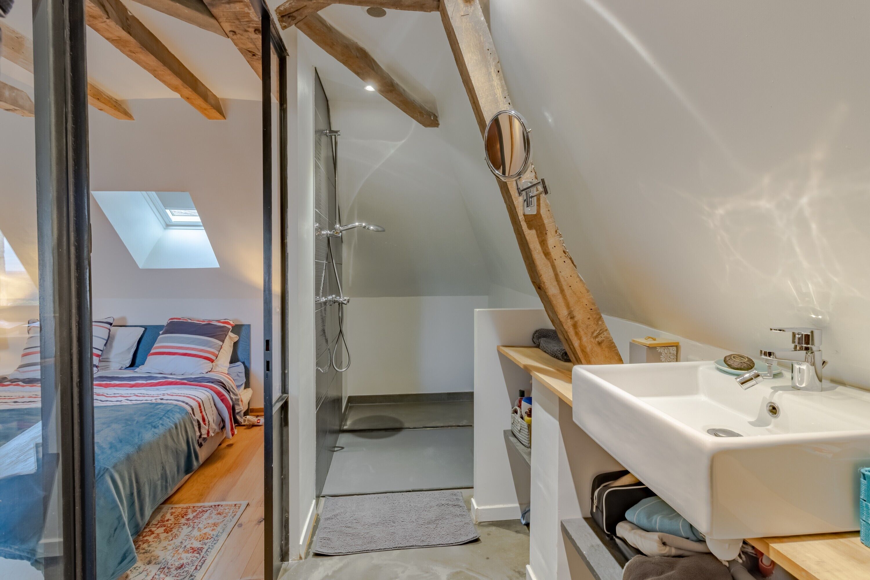 A bedroom with a skylight, a shower, a sink, and a bed with a view of the outside.