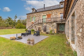 Una casa de piedra con un patio, mobiliario exterior y una escalera que conduce a un segundo piso.