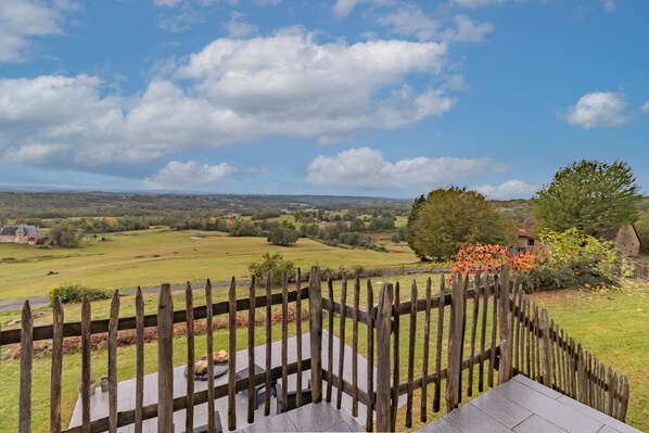Une terrasse en bois offrant une vue sur un paysage rural, avec des champs et des bâtiments situés au loin.