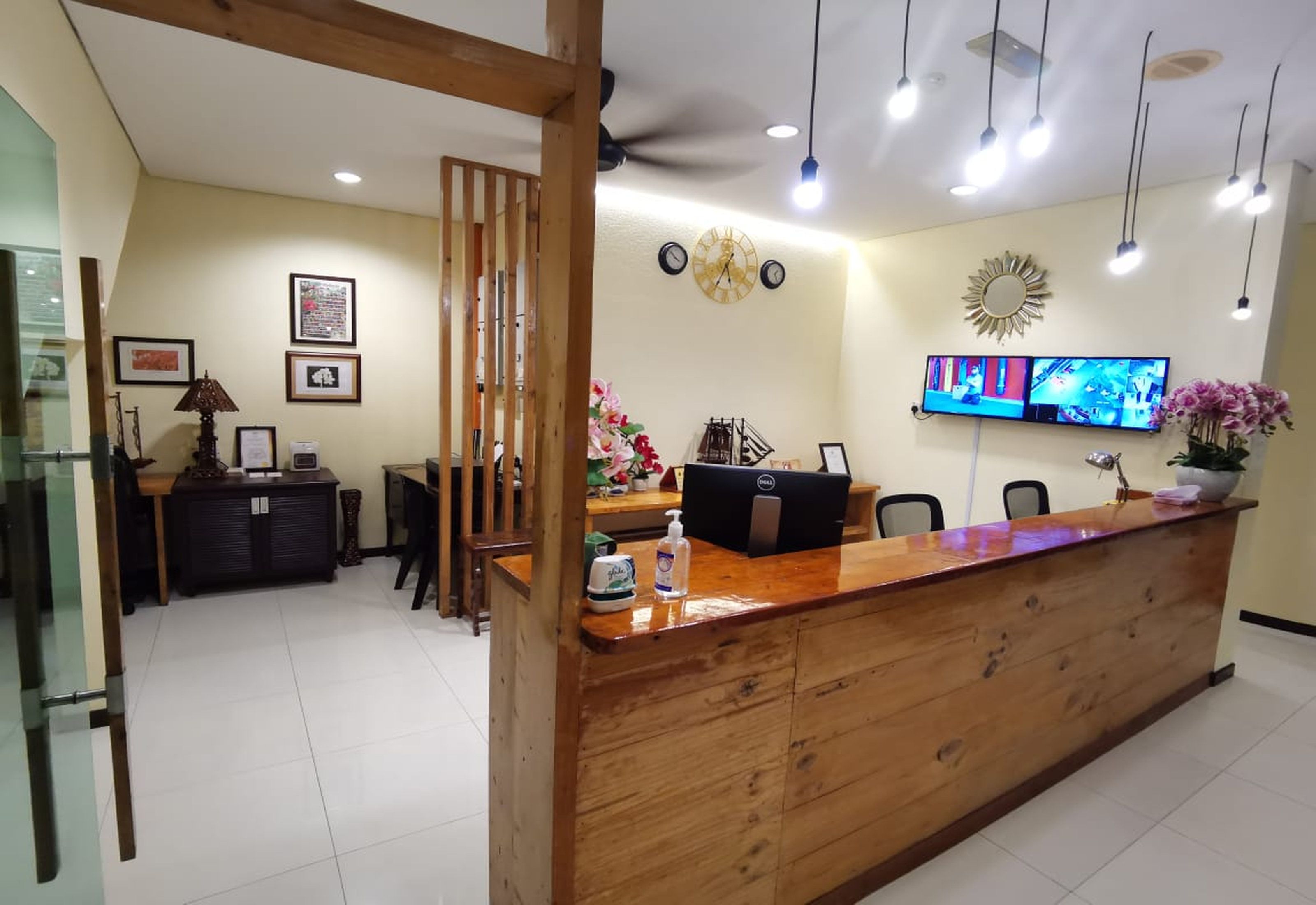 A reception area with a wooden desk, a computer, a clock, and a television displaying a news channel.