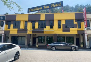 A two-story building with a sign reading 'Pavillion Inn Hotel.' There are two cars parked in front, and the building has a flat roof with a dark-colored awning. - Hotel O Pavilion Inn Hotel (Lumut)