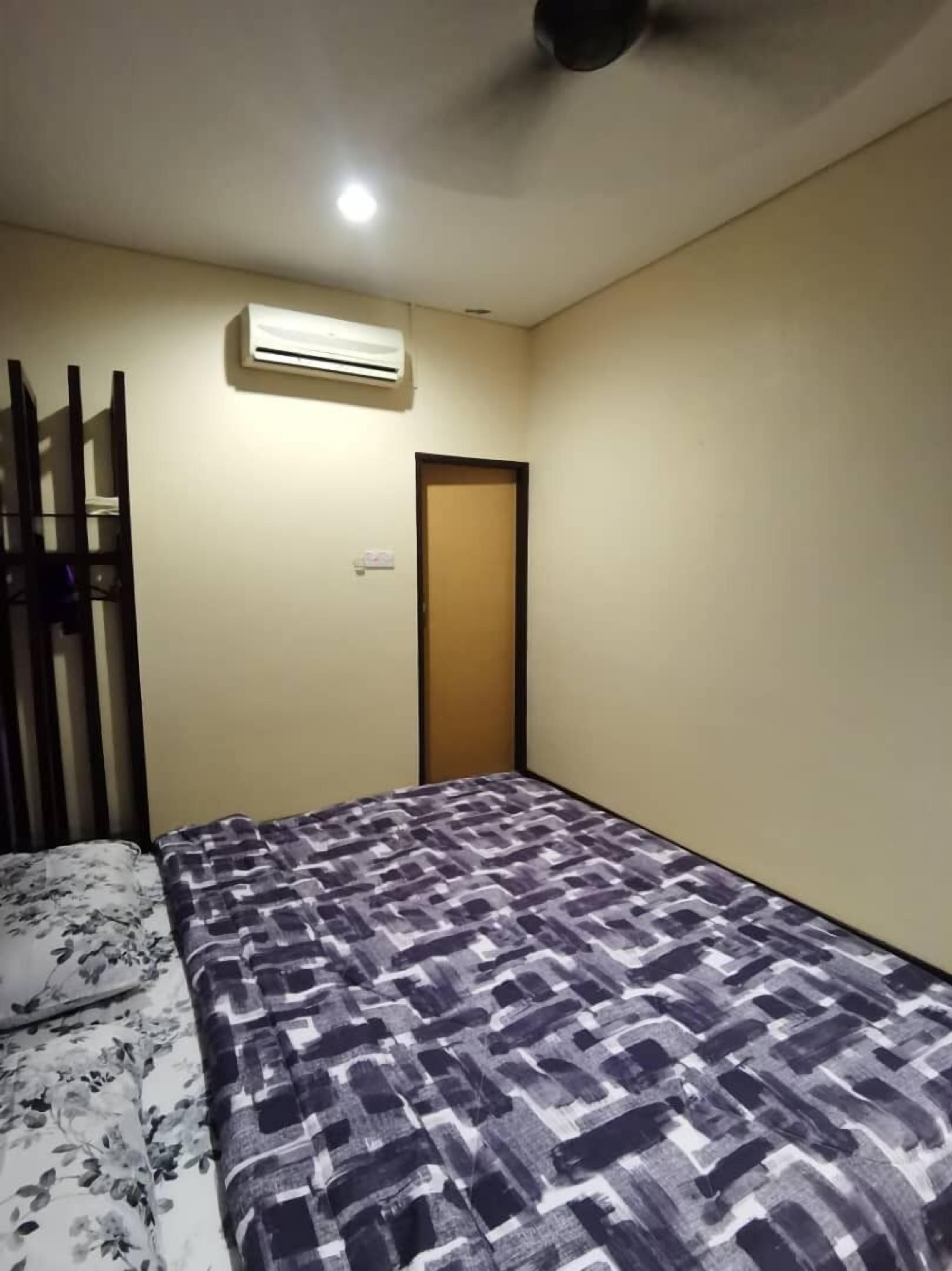 Une petite chambre d’hôtel composée d’une seule pièce, avec un lit, un appareil de climatisation, une porte et un ventilateur de plafond.