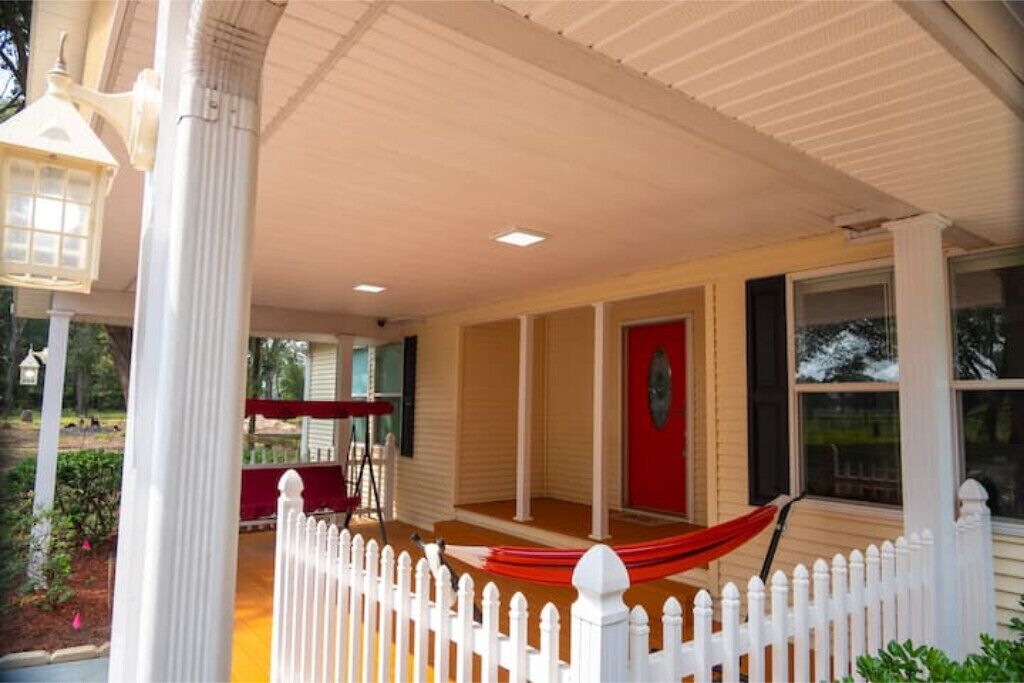 A covered porch with a white picket fence, a red door, and a hammock.