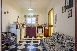 Un espacio habitable pequeño con kitchenette, piso a cuadros, un sofá y una silla de comedor.