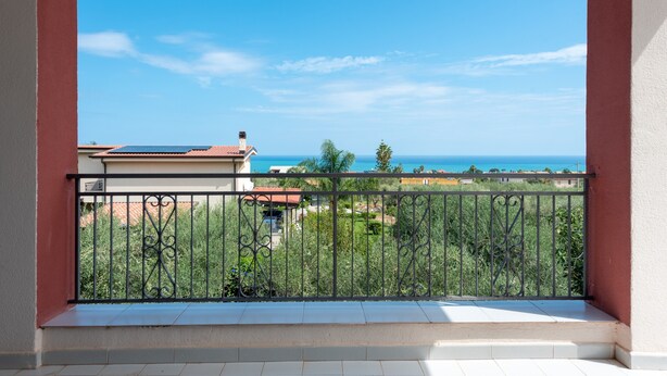 Ein Balkon mit Metallgeländer, der auf einen Garten und den Meerblick blickt.