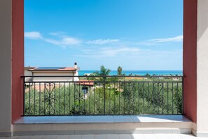 Un balcón con barandilla metálica que da a un jardín y vistas al mar.