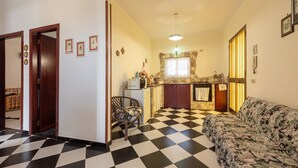 Ein Wohnzimmer mit Schachbrettmuster-Boden, einer Couch, einem Sessel, einer Küchenzeile mit Steinrückwand und einer Tür zu einem anderen Raum.