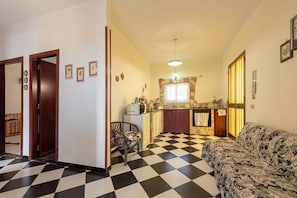 A living room with a checkered floor, a sofa, a chair, a kitchen area with a stone backsplash, and a doorway leading to another room. - Vacation Home "Zina" with Sea View, 2 Private Terraces & 2 Balconies (Altavilla milicia)