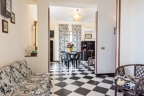Una sala de estar con piso a cuadros, un sofá, una mesa de comedor con sillas y un candelabro.