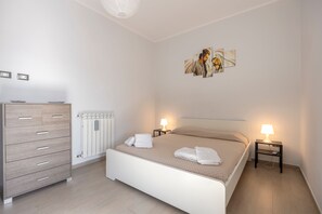 A hotel room with a bed, a dresser, a radiator, and a wall-mounted artwork.