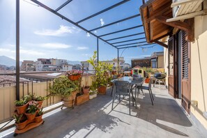 A balcony with a glass enclosure, potted plants, a table with chairs, and a view of the cityscape.