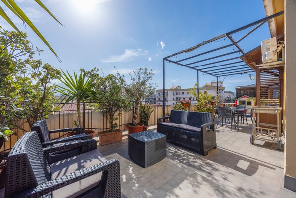 An outdoor patio area with wicker furniture, potted plants, and a pergola structure.