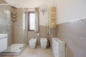A modern bathroom with a glass-enclosed shower, a bidet, a toilet, and a white sink.