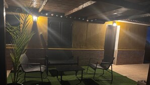 An outdoor patio with a table and chairs, a potted plant, and a wall with a light fixture.